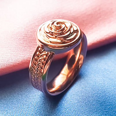 Custom rose gold rose signet ring resting on pastel pink and blue fabric